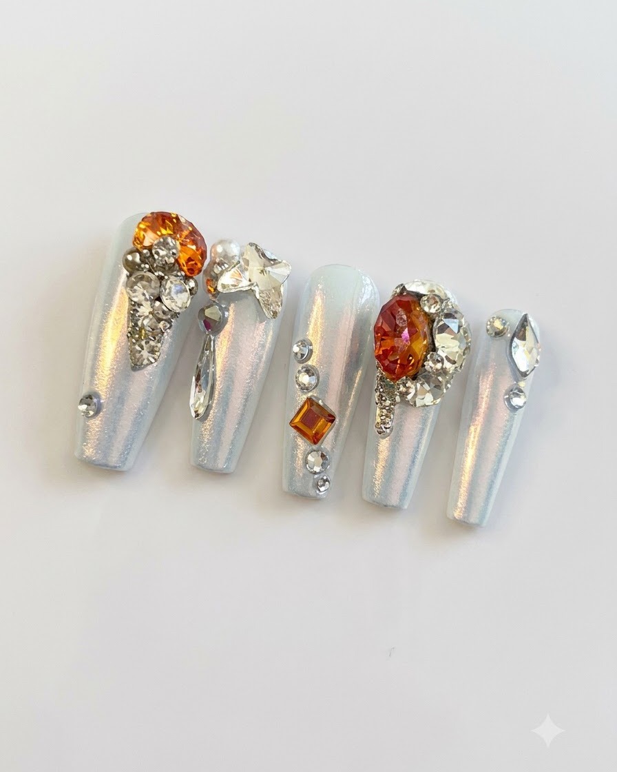 Une photo macro rapprochée montrant de fines billes dargent, de petits strass et des breloques papillon regroupés sur les ongles press-on.