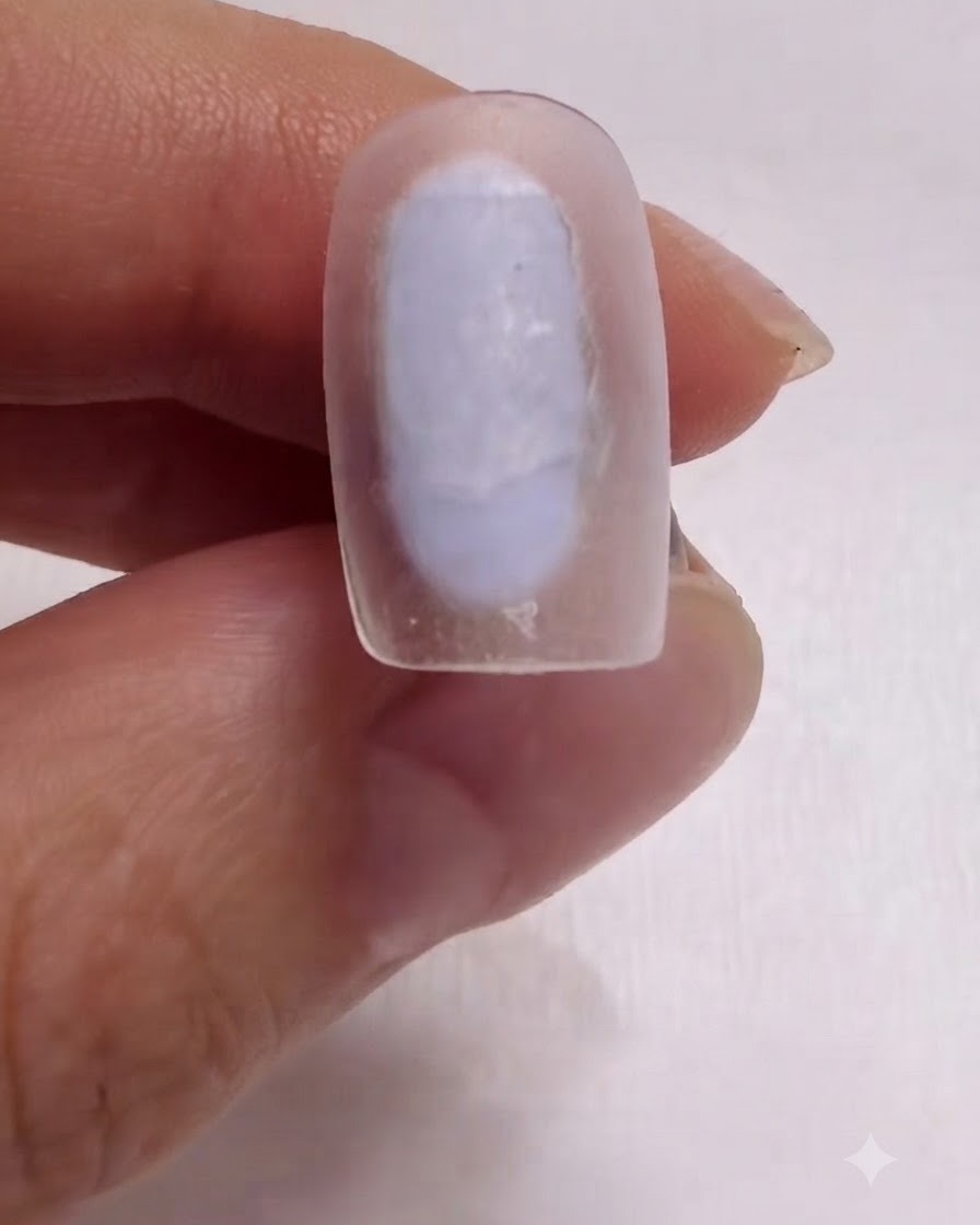 Un pinceau appliquant soigneusement une couche de base blanc lait sur la surface dun ongle.