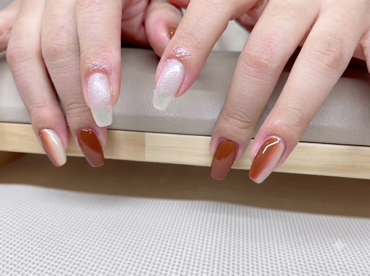 Gros plan de mains montrant une manucure en dégradé caramel et ambre avec des lignes de reflets cat-eye lumineuses.