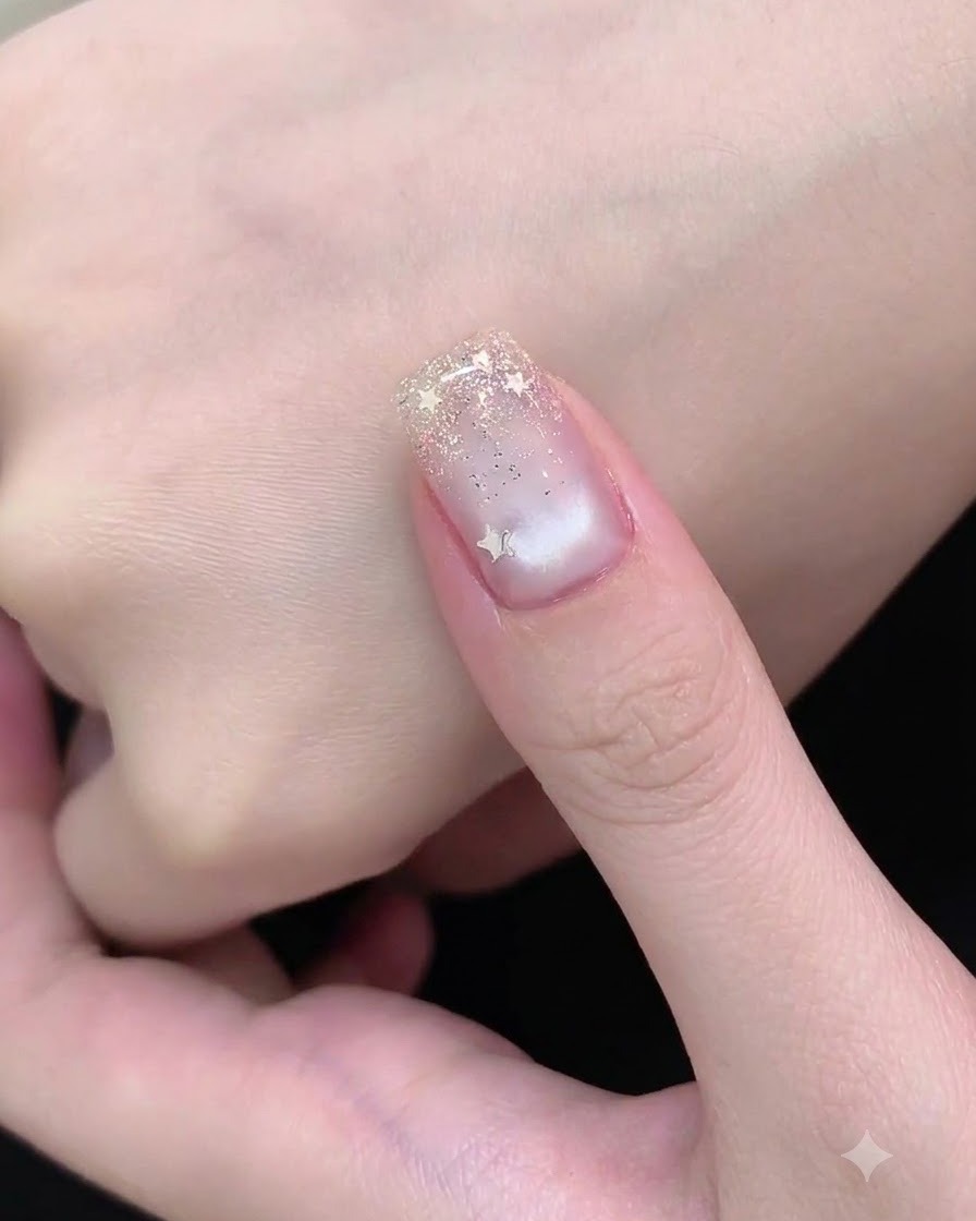 Un pinceau de nail art appliquant de fines paillettes argentées sur le bord libre de longle pour former un dégradé.