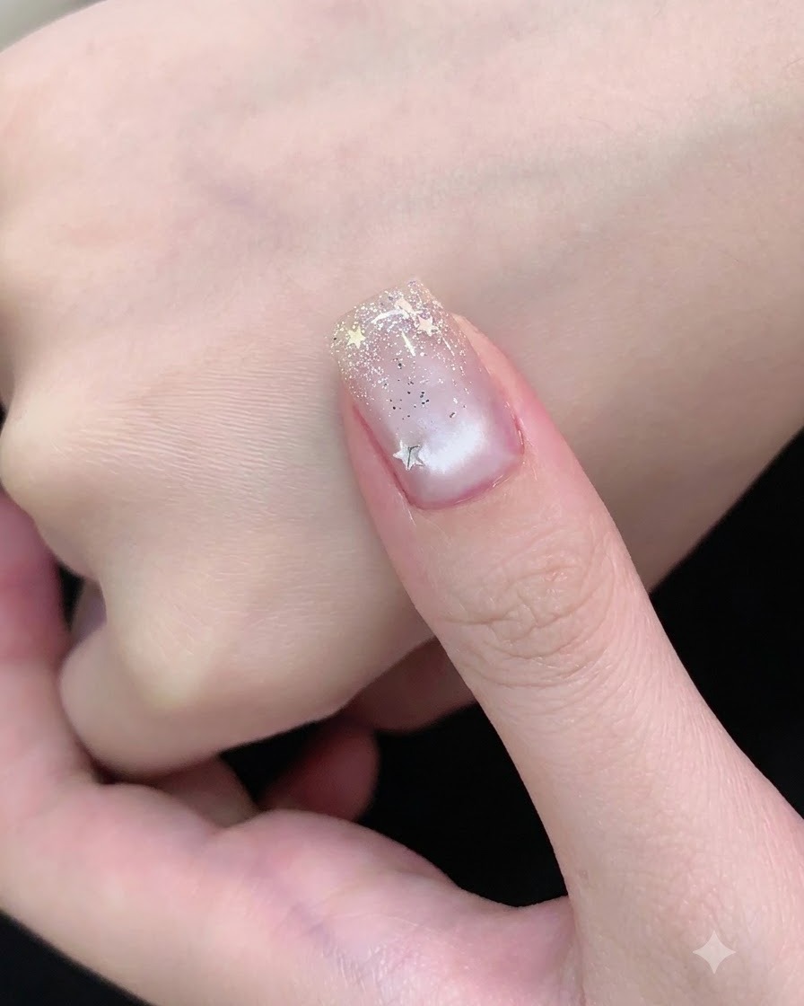 Un pinceau à ongle appliquant un top coat transparent sur un ongle décoré de paillettes argentées et détoiles.