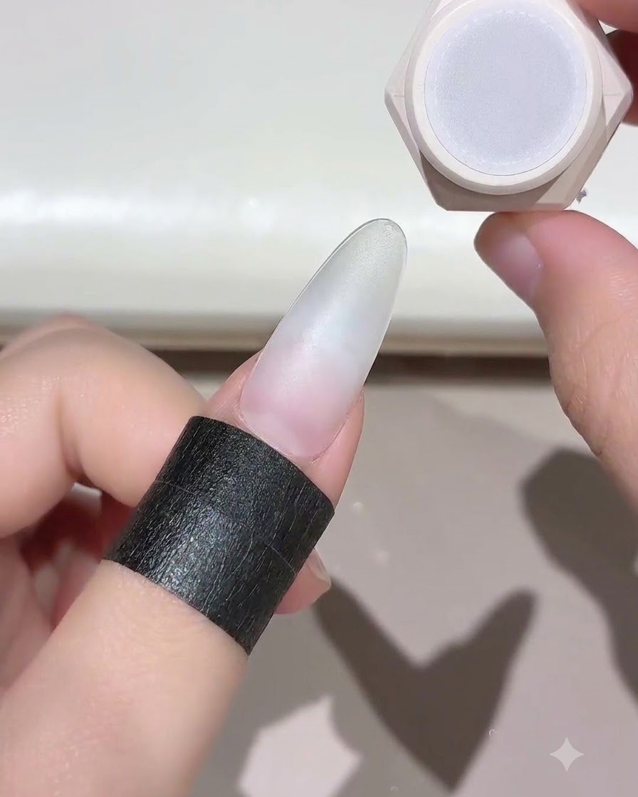 Un doigt avec un ongle préparé maintenu près dun pot de gel pour ongles, prêt pour la catalysation.