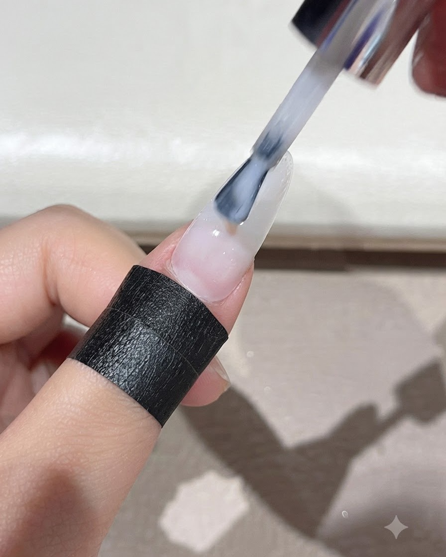Un pinceau étalant uniformément du gel auto-égalisant blanc laiteux sur toute la surface de longle.