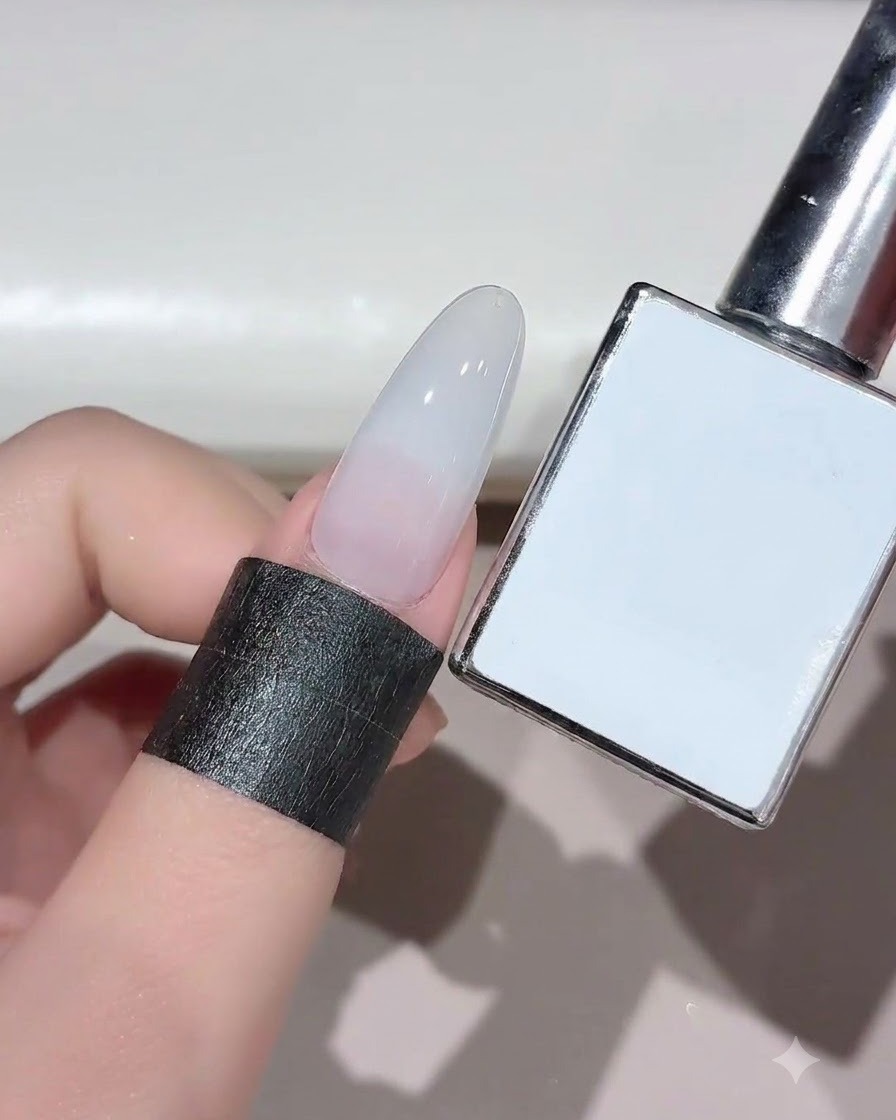 Un ongle avec du gel blanc laiteux catalysé présenté à côté de son flacon de produit.