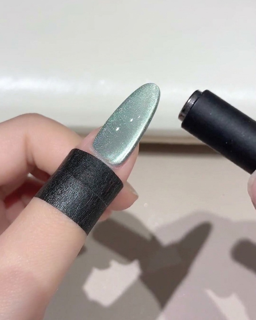 Un outil magnétique noir survolant un ongle œil-de-chat vert scintillant pour façonner la bande lumineuse.