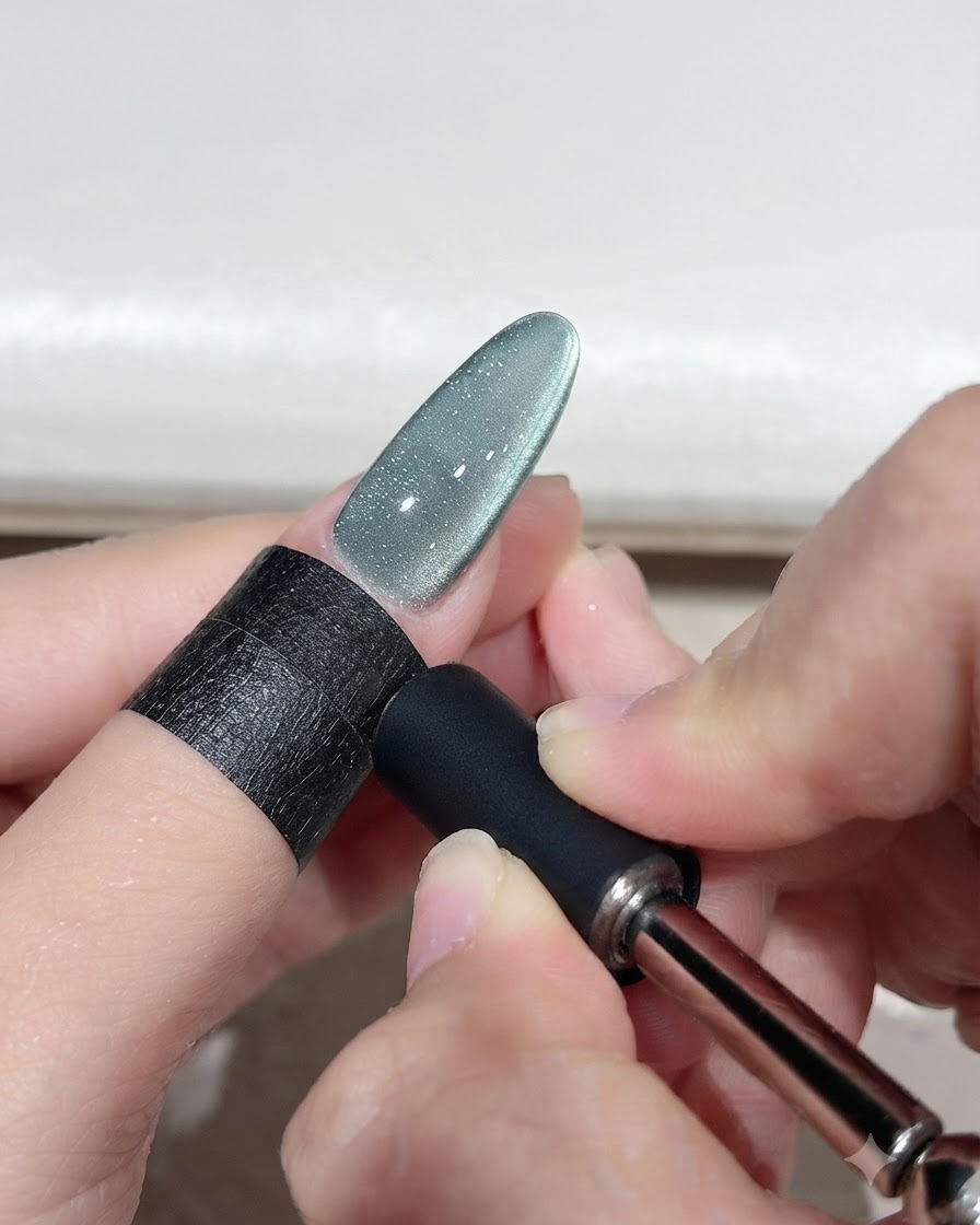 Un outil magnétique tenu près dun ongle en gel œil-de-chat vert pour façonner un arc lumineux incurvé.