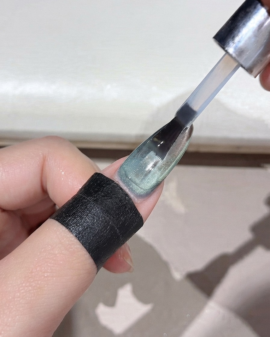 Un pinceau à ongles appliquant un top coat transparent sur un ongle vert en dégradé avec fini miroir.