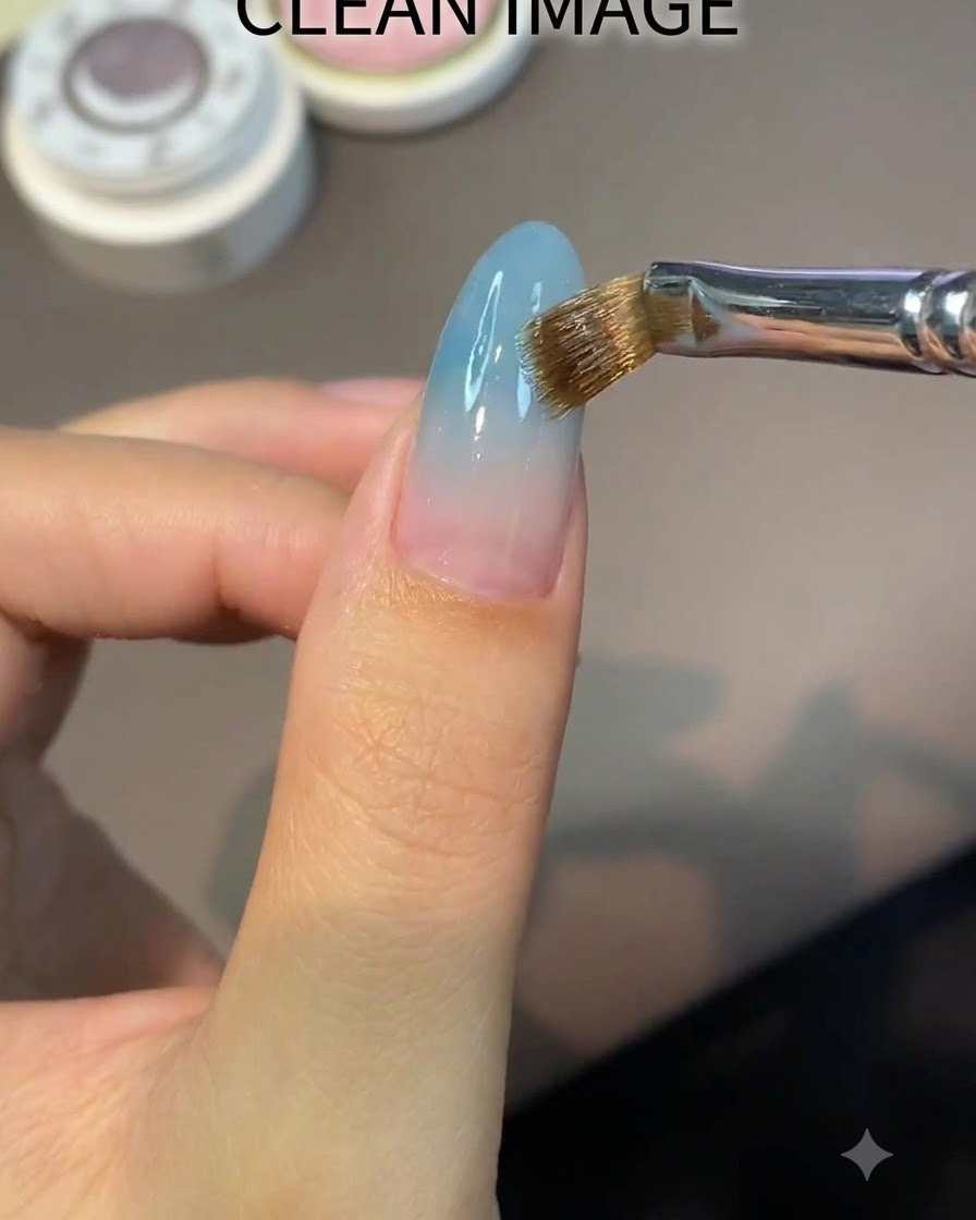 Un pinceau plat appliquant uniformément un gel de base nude transparent sur un ongle en amande.