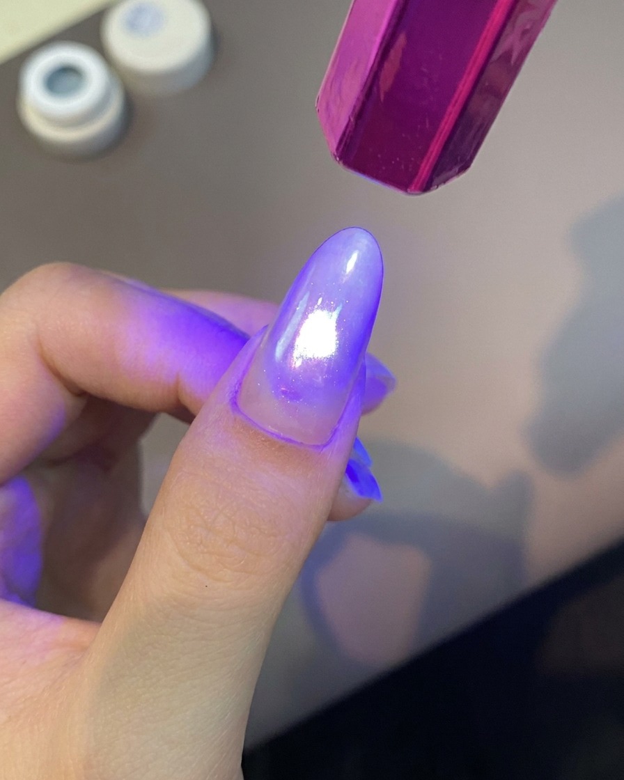 Une lampe UV portative violette éclairant vivement un doigt manucuré pour catalyser le revêtement en gel.
