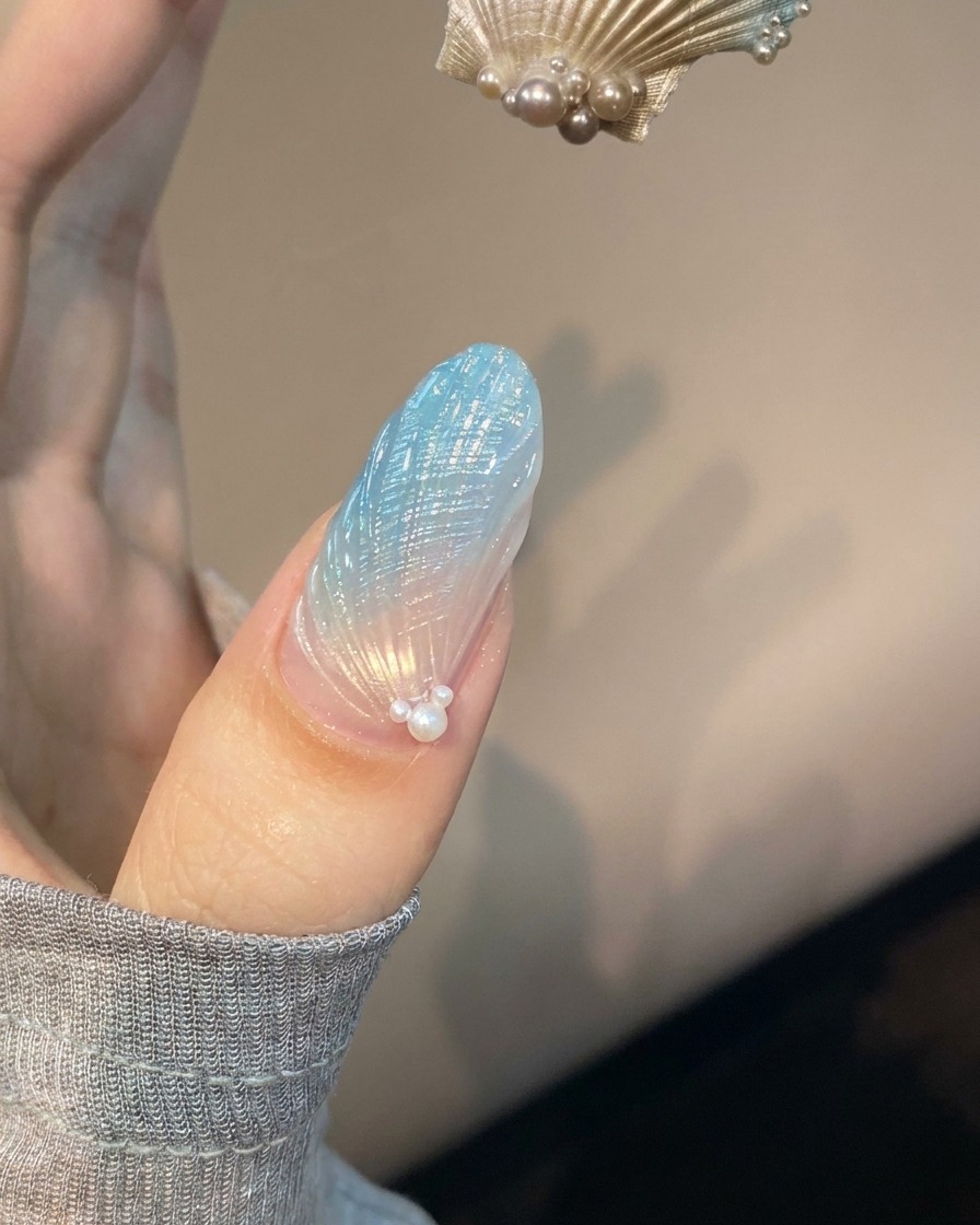 Un onglet avec un nail art coquillage bleu et translucide placé sous une lampe UV violette en train de catalyser.
