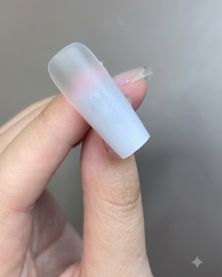 Une fine couche de gel blanc laiteux appliquée au pinceau sur la surface de longle en dégradé.