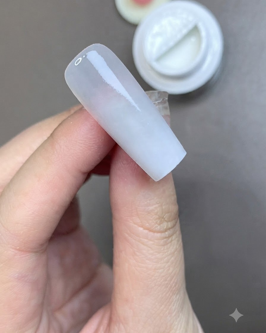 Un pinceau appliquant une couche lisse de top coat mat sur un ongle préparé en blanc laiteux.