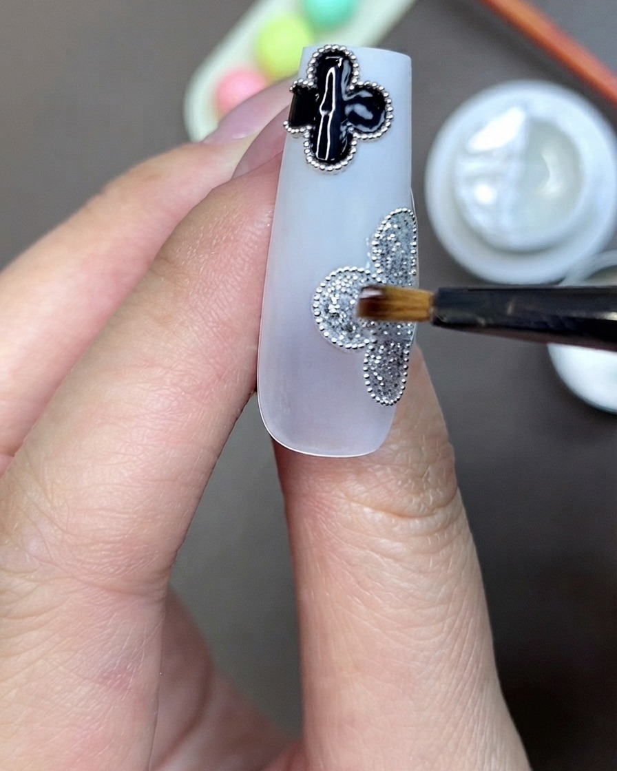 Un pinceau appliquant du gel adhésif transparent pour strass au centre dun motif de trèfle pailleté argenté sur un ongle.