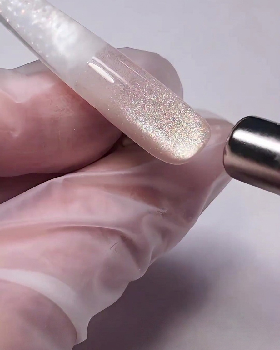 Un bâtonnet aimanté cylindrique maintenu près du gel cat-eye humide sur un ongle, attirant les particules métalliques pour former un reflet.