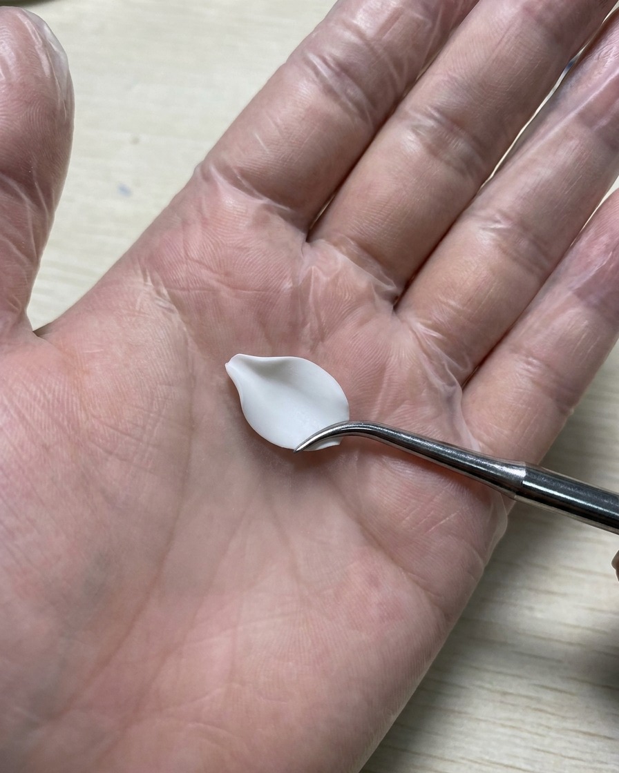 Une main gantée tenant un outil de modelage en silicone lissant un pétale de gel 3D blanc posé sur un tapis en silicone.