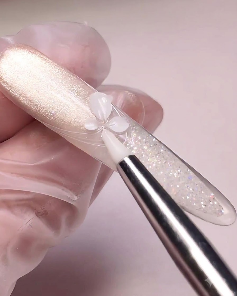 Un outil en silicone pressant du gel de sculpture blanc pour former des pétales de fleur sur un ongle habillé dun cat-eye.