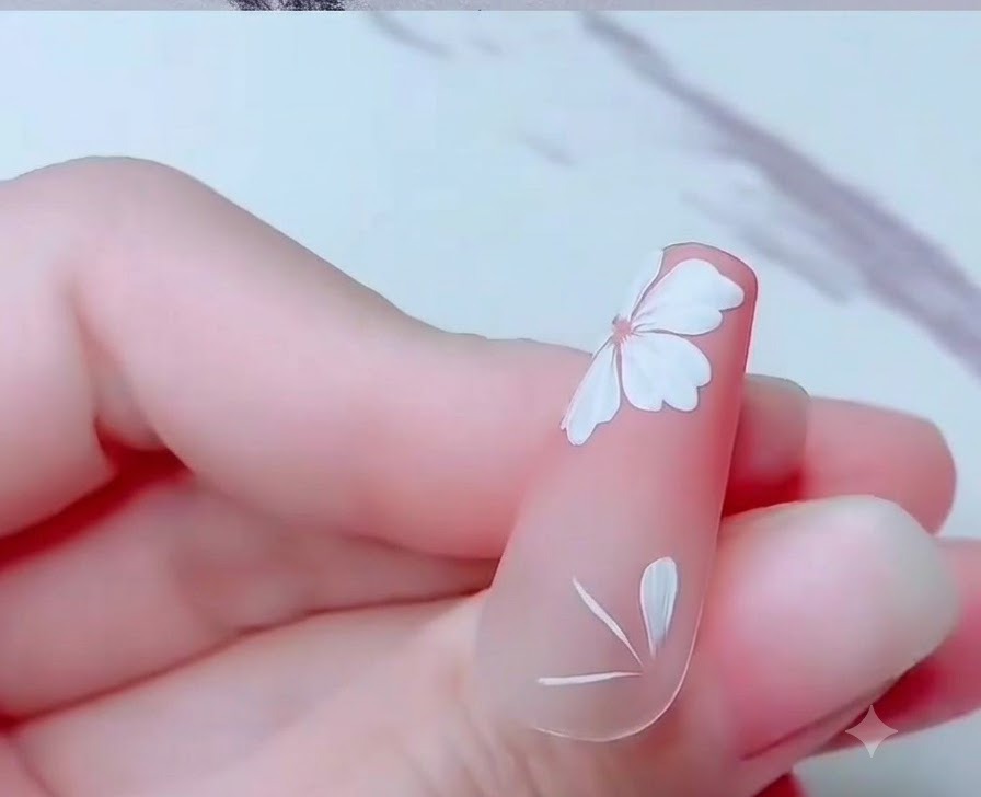 Gros plan dun ongle montrant des pétales partiels de fleurs de cerisier blanches peints près du bord inférieur.