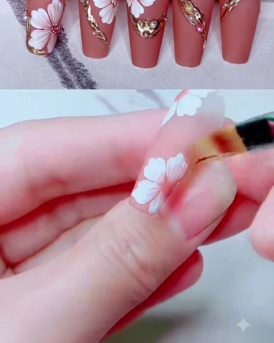 Un petit pinceau dégradeur estompant la couleur rose sur des pétales de fleurs peints en blanc sur un ongle.