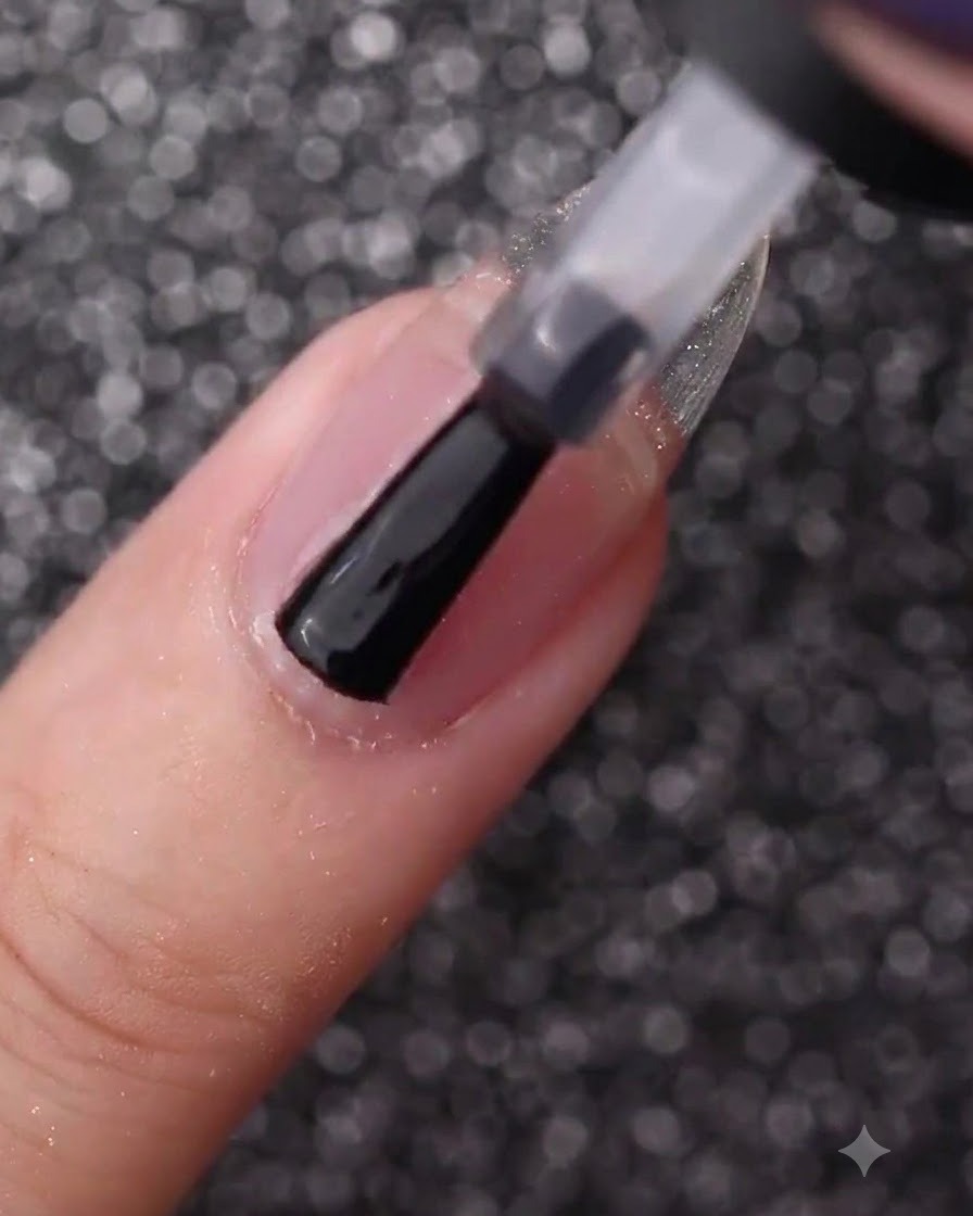 Une main utilisant un pinceau de flacon pour enduire un ongle naturel nu de gel de base transparent.
