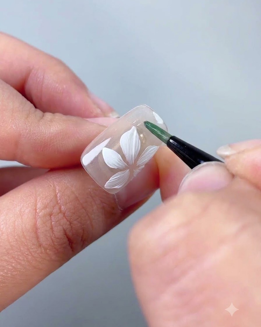 Un pinceau liner appliquant du gel vert pour former une fine feuille à côté de la fleur blanche.