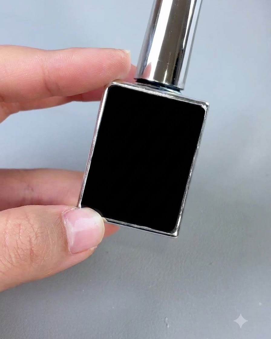 Un petit flacon cosmétique noir avec un bouchon argenté et un pinceau applicateur, présenté verticalement sur un fond gris.