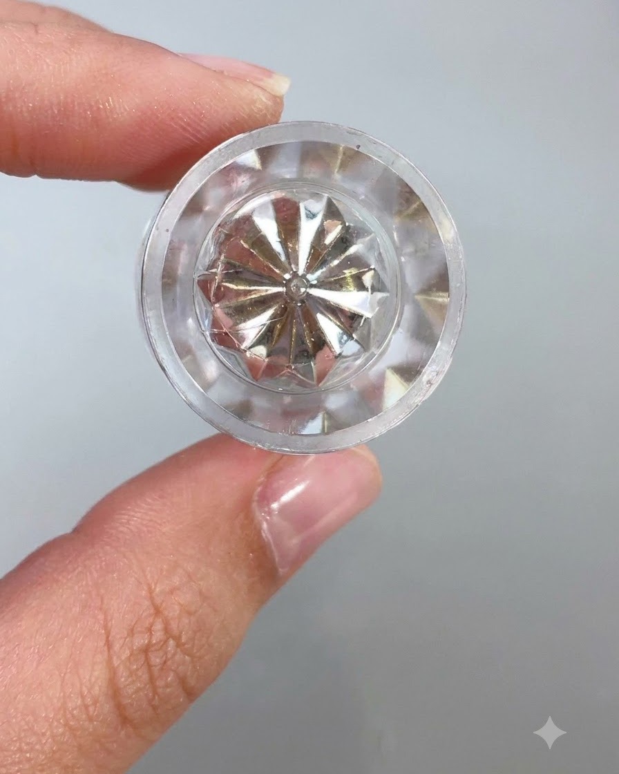 Vue rapprochée dun haut de récipient en cristal transparent et à facettes ou dun outil applicateur reflétant la lumière sur un fond clair.