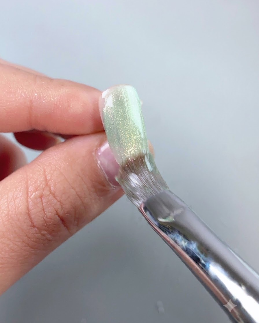 Un pinceau à ongles lissant une couche de gel cat-eye vert transparent sur la surface dun faux ongle.