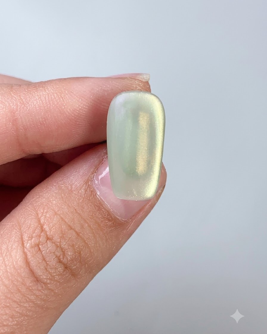 Un pinceau à ongles appliquant un top coat sur un ongle en gel cat eye vert.