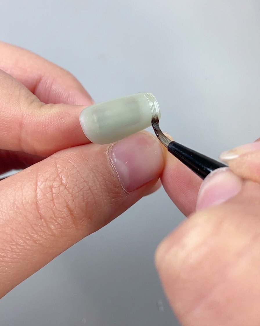 Un pinceau de détail fin utilisant du gel de modelage de texture transparent pour tracer une bordure en relief le long du bord dun ongle cat eye.