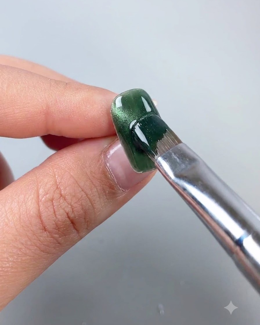 Une baguette magnétique tenue près dun ongle en gel cat eye vert pour déplacer les particules magnétiques dans une ligne en arc latéral.