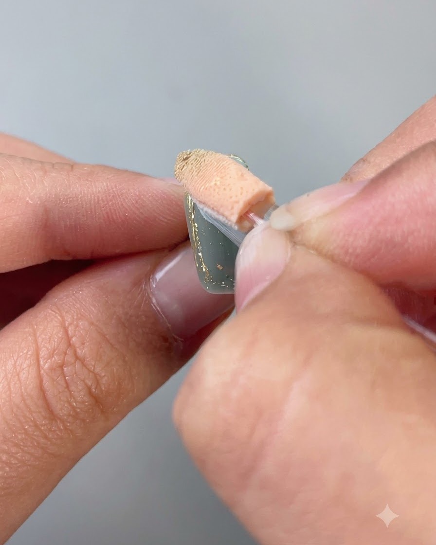 Un applicateur éponge frottant de la poudre dorée sur le bord contouré dun ongle.