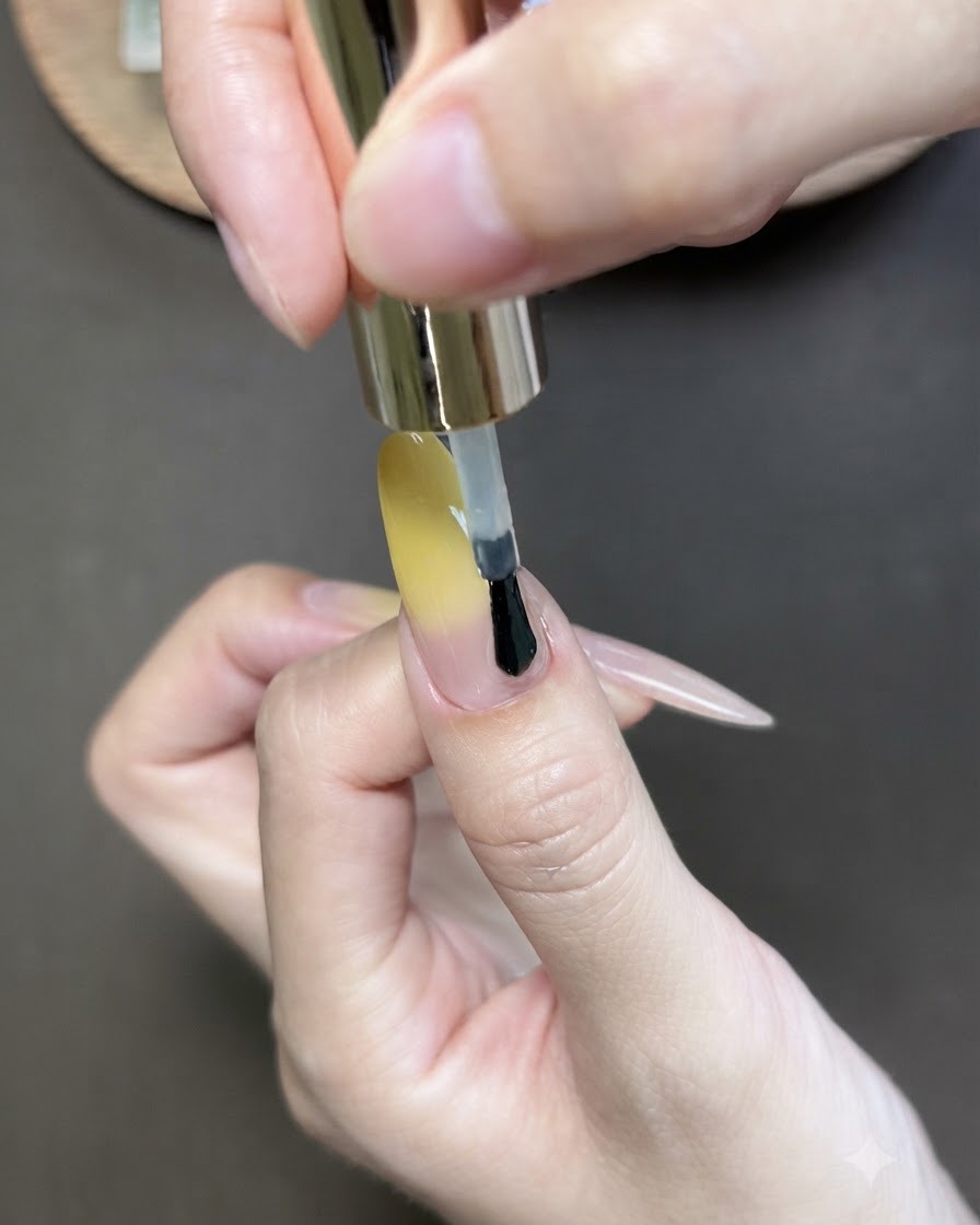 Un pinceau appliquant du vernis gel cat-eye sur longle du pouce au dégradé jaune.