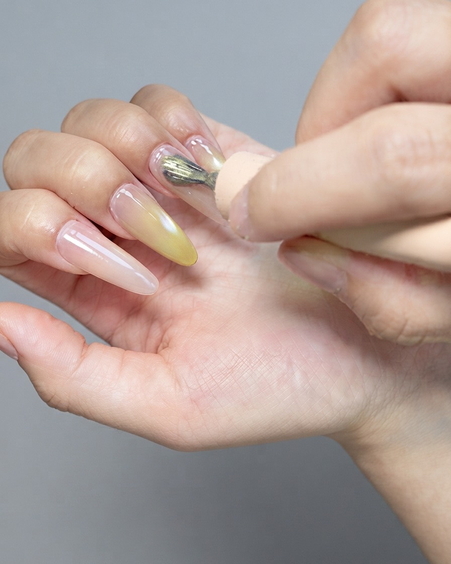 Un outil aimanté puissant survolant un ongle en gel cat-eye brillant pour façonner les particules magnétiques.
