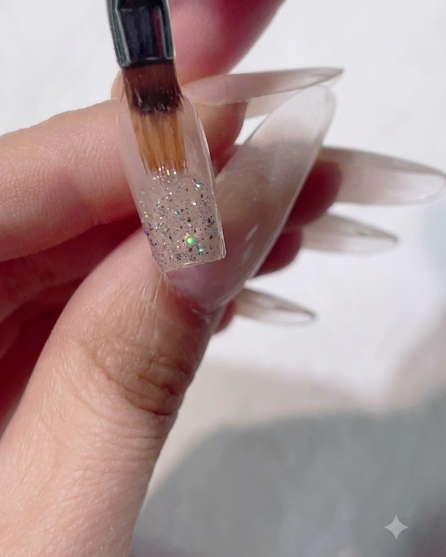 Un pinceau gel plat balayant des paillettes humides vers le bas sur un ongle pour créer un effet dégradé ombré.