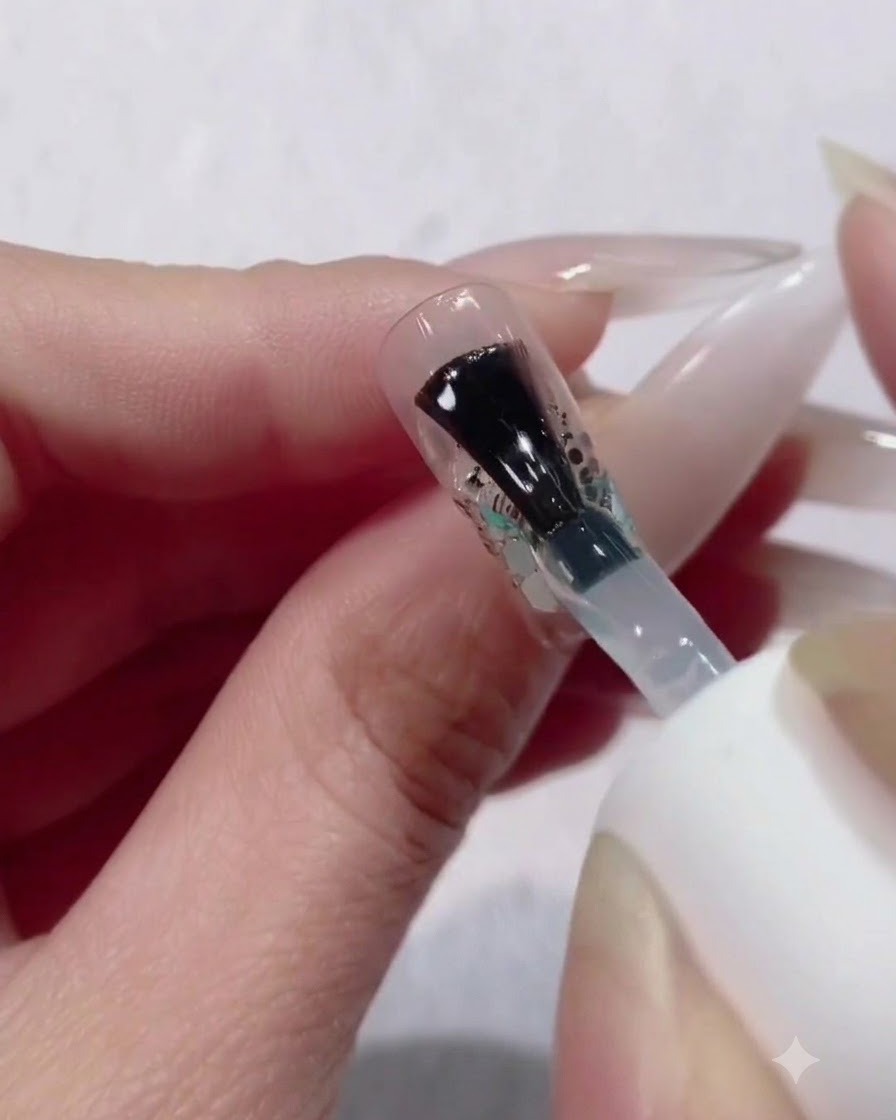 Un pinceau de flacon appliquant une couche épaisse et généreuse de gel de construction transparent sur un design dongle en dégradé de paillettes et sequins.