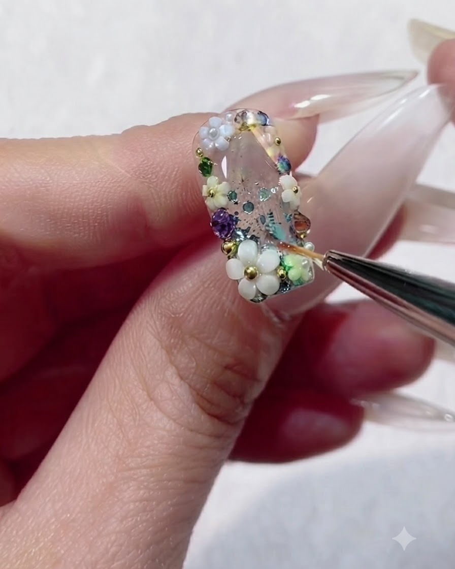 Un pinceau liner remplissant les minuscules espaces entre des strass colorés et des perles sur un ongle en gel transparent.