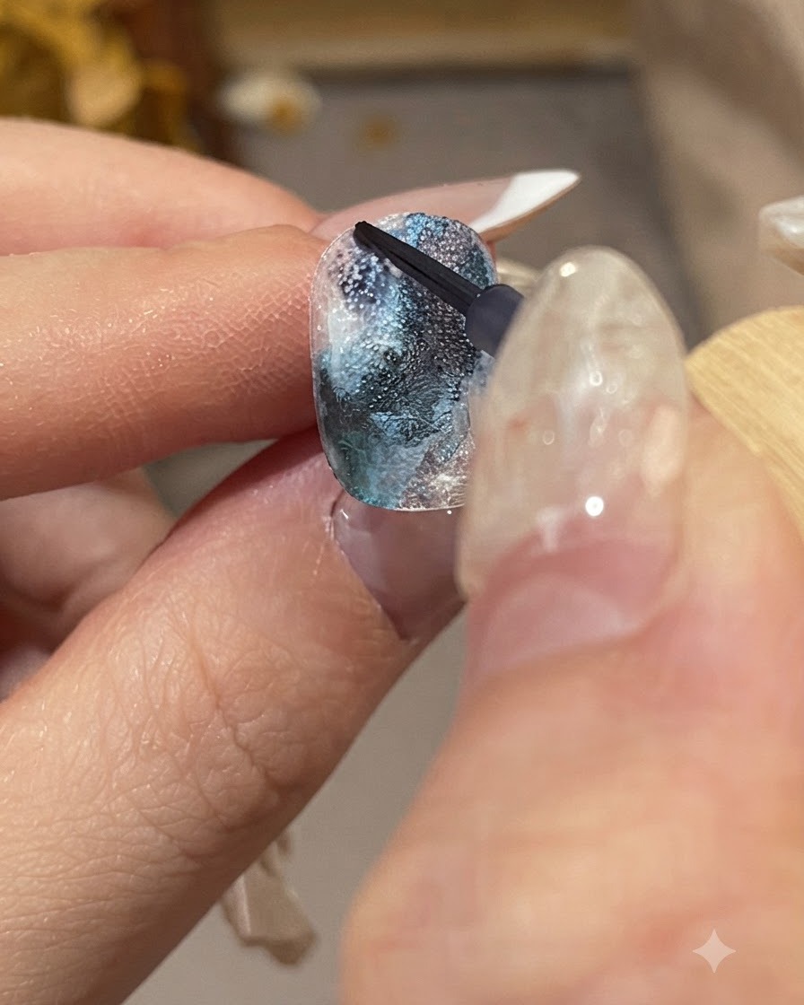 Gros plan détaillé dune main manucurée tenant un pinceau fin pour appliquer des gouttes dencre bleu foncé sur une surface dongle texturée.