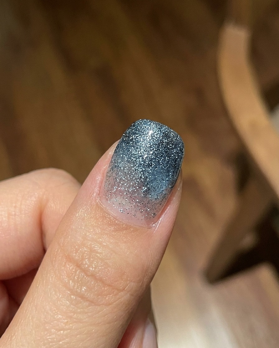 Un doigt arborant une couche de dégradé en gel jelly bleu translucide sur un fond texturé pailleté, photographié sous une vive lumière naturelle.