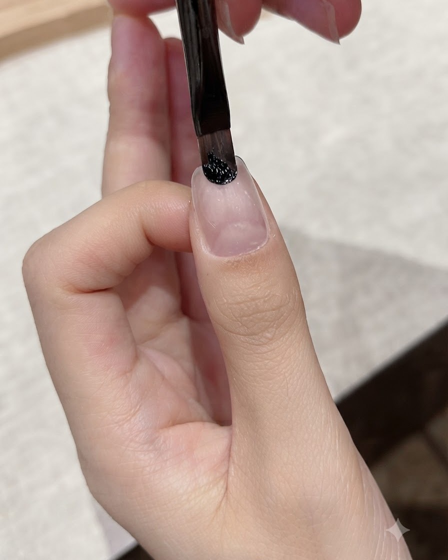 Un pinceau fin appliquant du gel noir foncé près de la zone des cuticules dun ongle naturel.