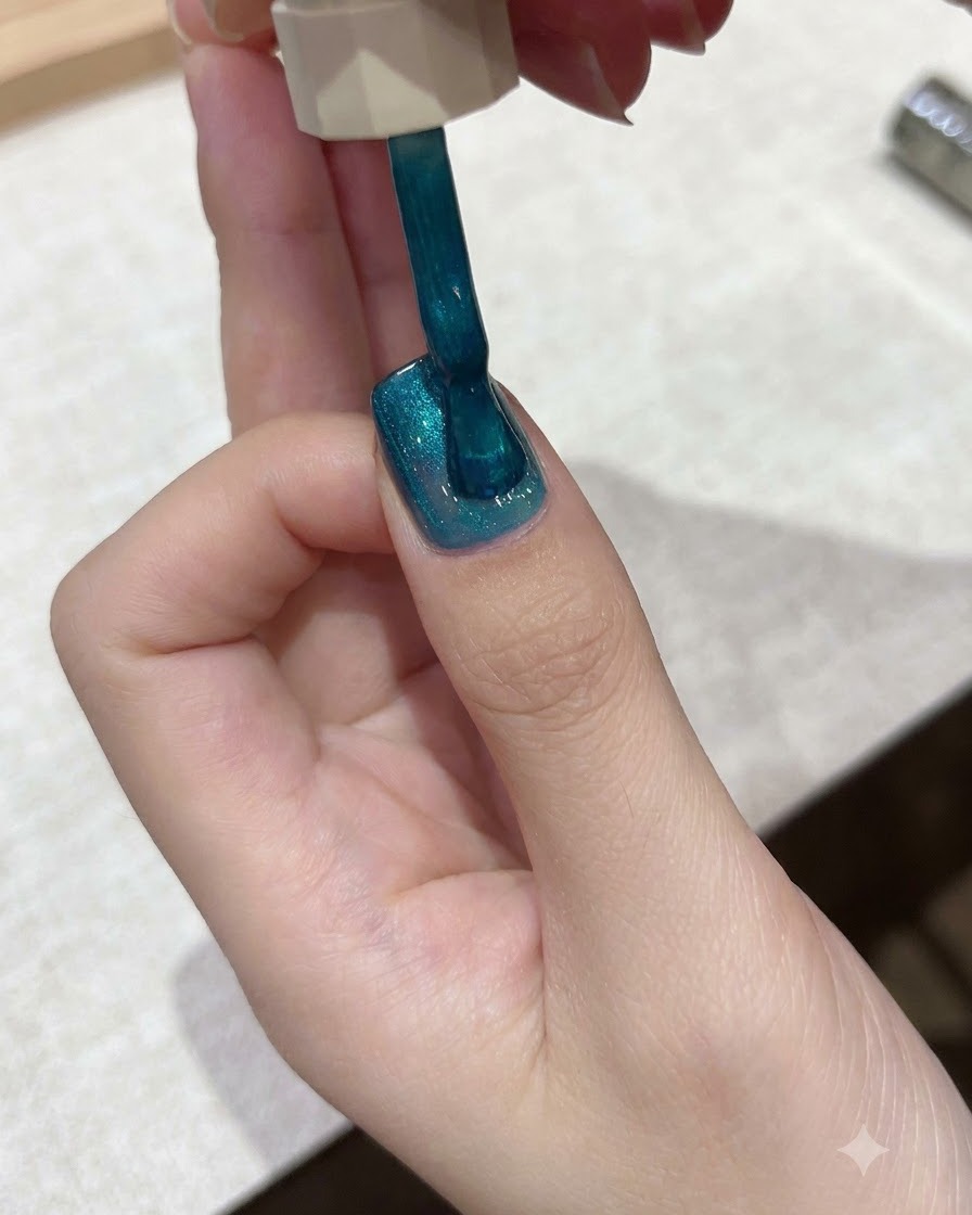 Un pinceau appliquant du vernis gel cat-eye bleu sarcelle vibrant sur la surface dun ongle.