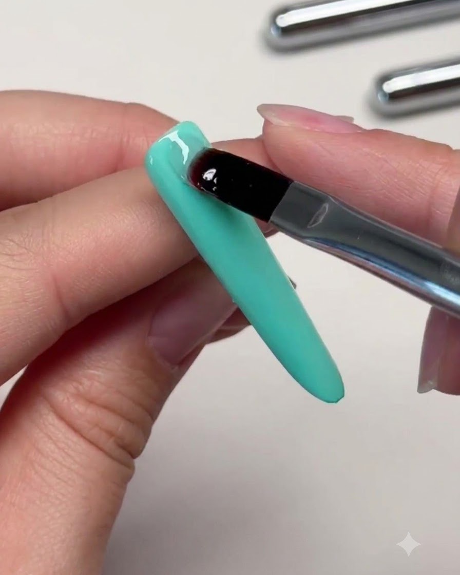 Un pinceau plaquant une perle transparente de gel de renfort sur la partie supérieure dun ongle vert menthe pour créer un apex.