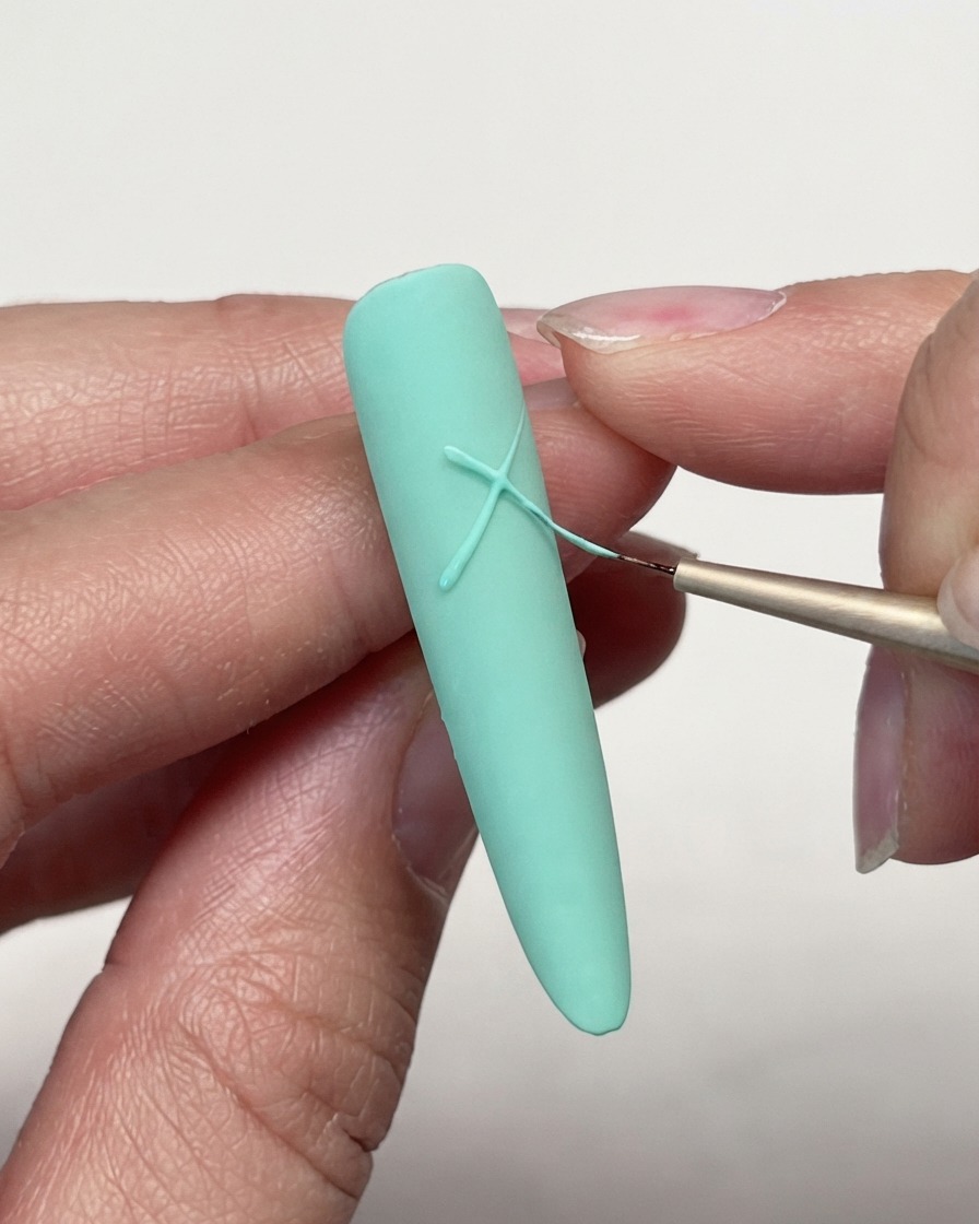 Gros plan dun pinceau liner croisant des lignes de gel sur le bout dun ongle mat vert menthe pour commencer un motif détoile.