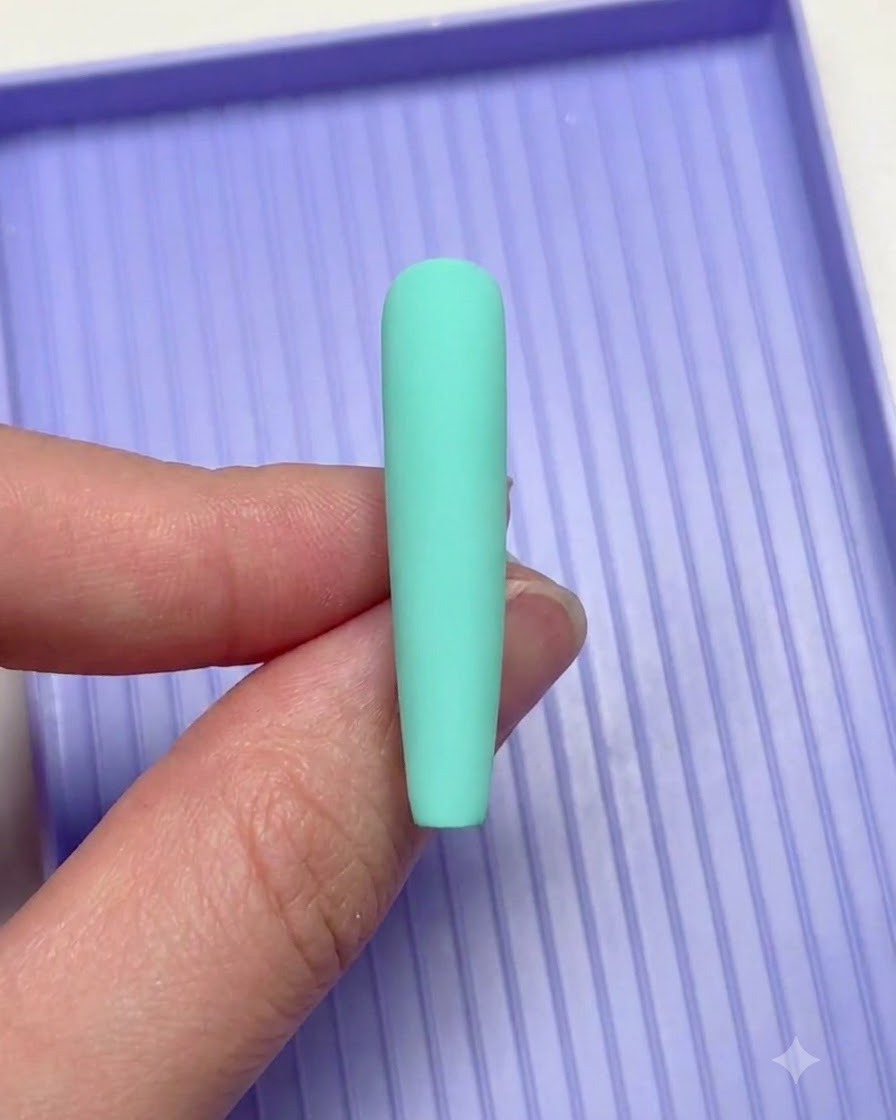 Une main tenant un ongle vert menthe au-dessus dun plateau de tri violet lors de la réalisation du nail art.