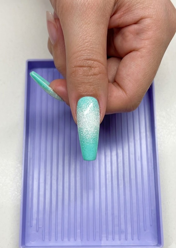 Une main tenant un long ongle vert menthe avec un design détoile sucrée blanche sous une lampe de catalysation UV LED violette.