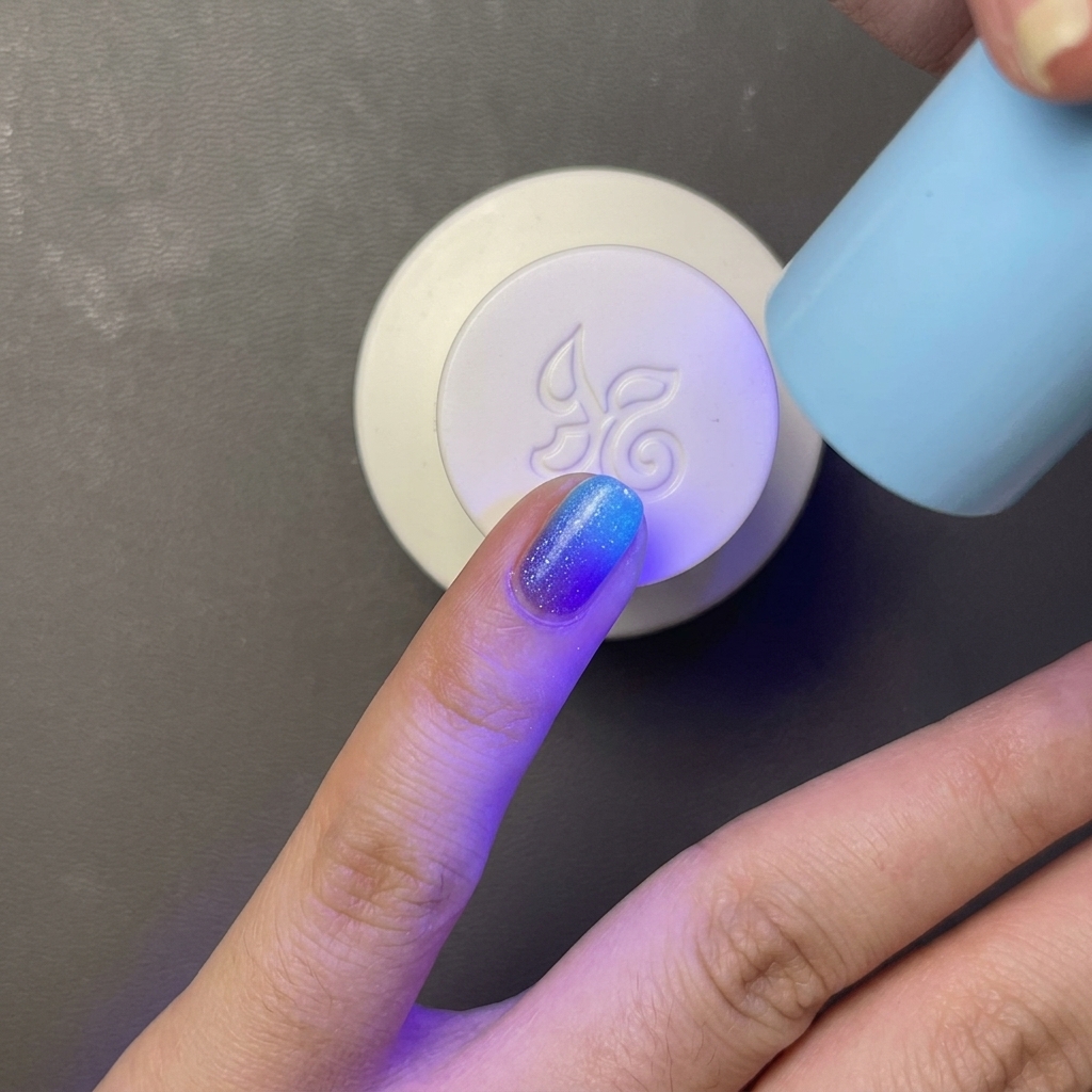 Un doigt avec un vernis gel bleu vif en train de catalyser sous une petite lampe UV/LED bleue portable.