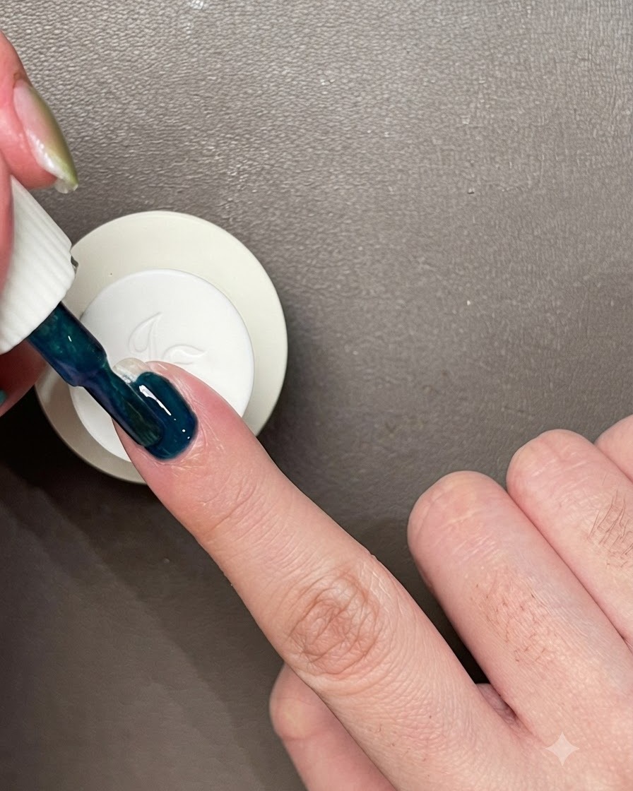 Application dune couche de vernis gel bleu-vert foncé directement sur un ongle naturel nu.