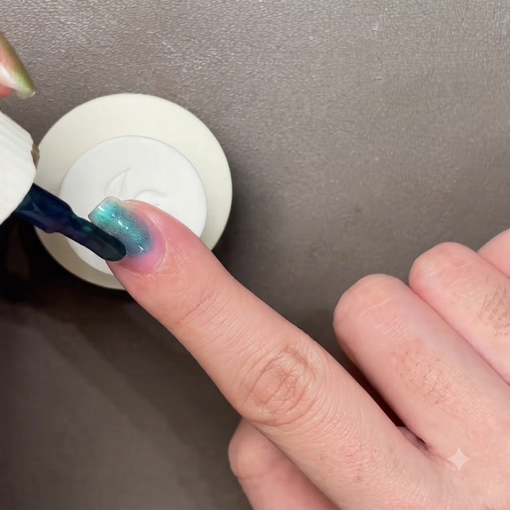 Un bâtonnet aimanté noir planant au-dessus dun ongle peint en bleu-vert foncé pour manipuler le vernis œil de chat.