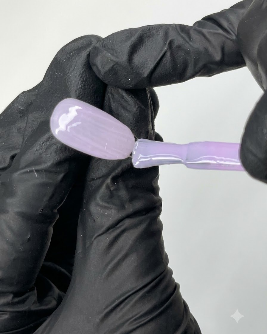 Un pinceau plat étalant uniformément le vernis gel violet diaphane N04 sur la surface dune capsule dongle dentraînement ovale.