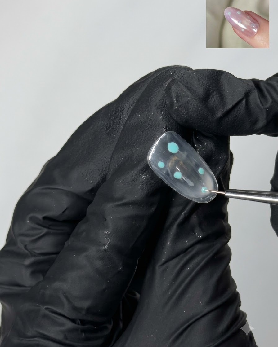 Un pinceau de détail fin plaquant de petits accents de points turquoise sur une surface dongle en gel transparent.