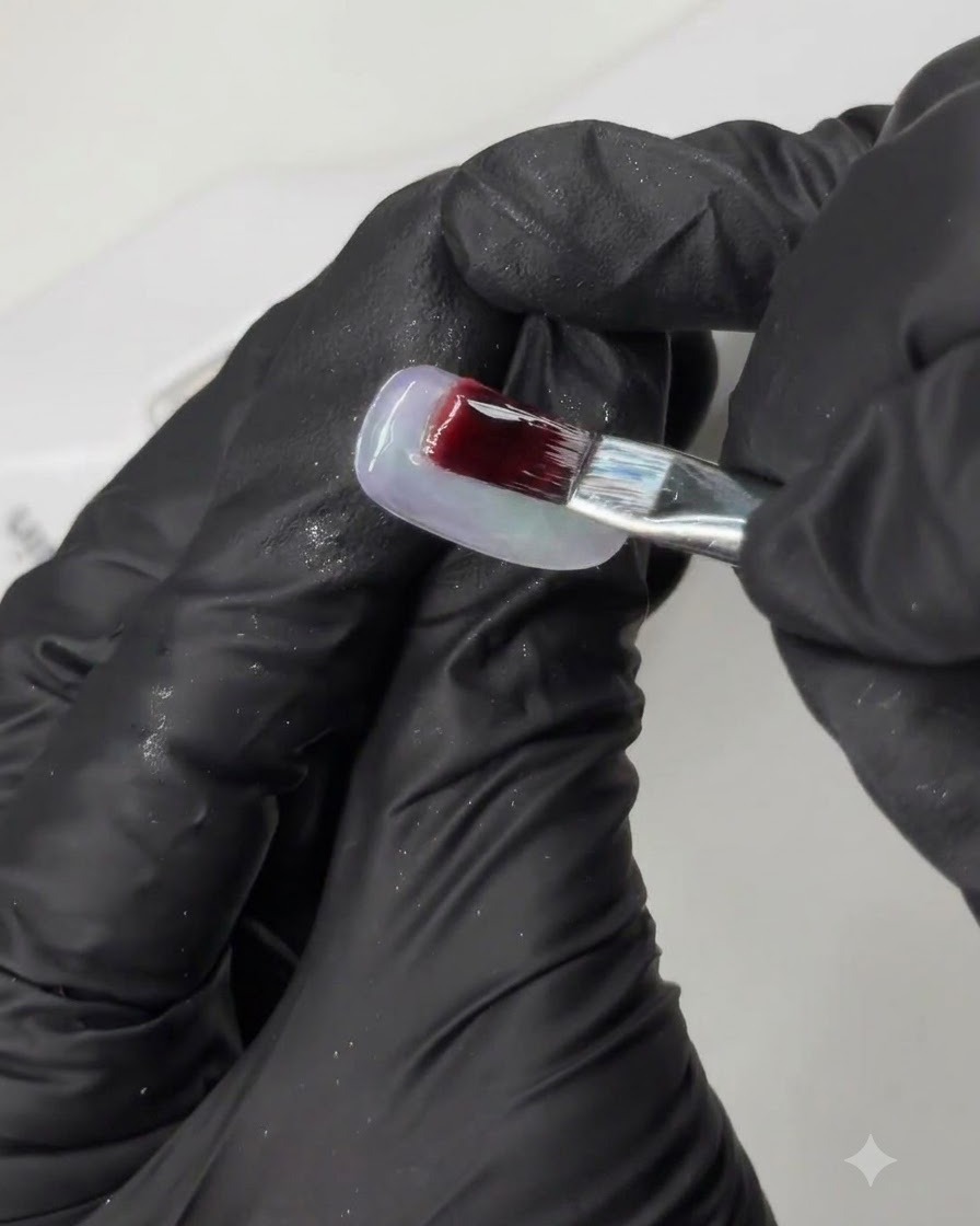 Un pinceau appliquant un gel hautement pigmenté sur une capsule dongle dentraînement lors dun tutoriel de nail art en plusieurs étapes.